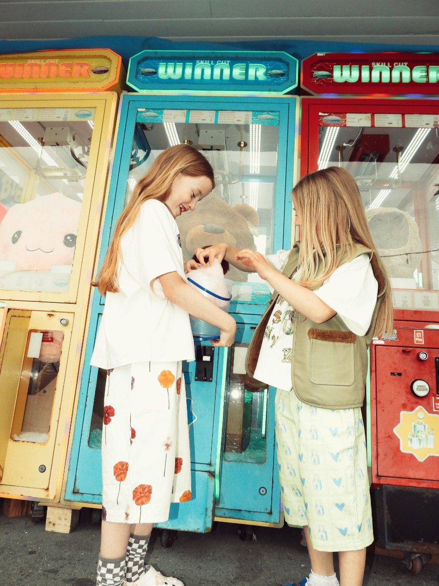 Amelia: T-Shirt und Hose von SAUCE MINI, Socken mit Schachbrettmuster von ZARA, Clogs mit Blumen von CROCS. Jessica: T-Shirt und Hose von SAUCE MINI, Lederweste von FILLE GARÇON, Spitzensöckchen MODEL’S OWN