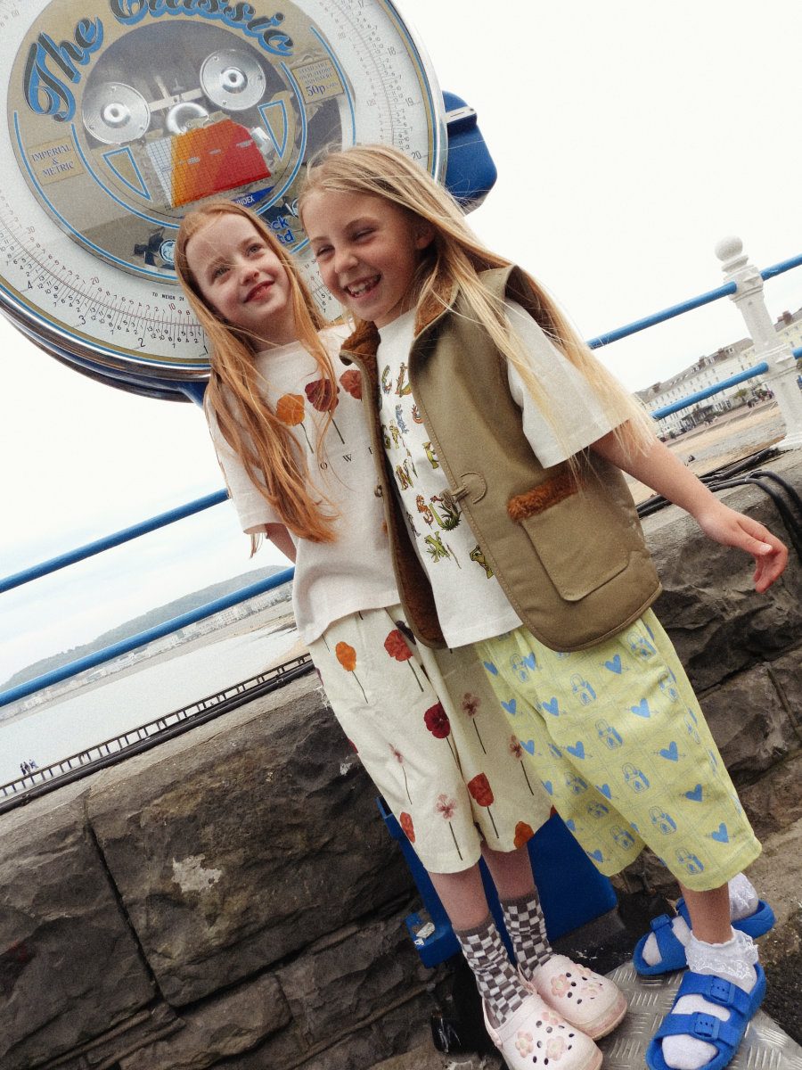 Amelia: T-Shirt und Hose von SAUCE MINI, Socken mit Schachbrettmuster von ZARA, Clogs mit Blumen von CROCS. Jessica: T-Shirt und Hose von SAUCE MINI, Spitzensöckchen MODEL’S OWN, Sandalen von MARKS & SPENCER